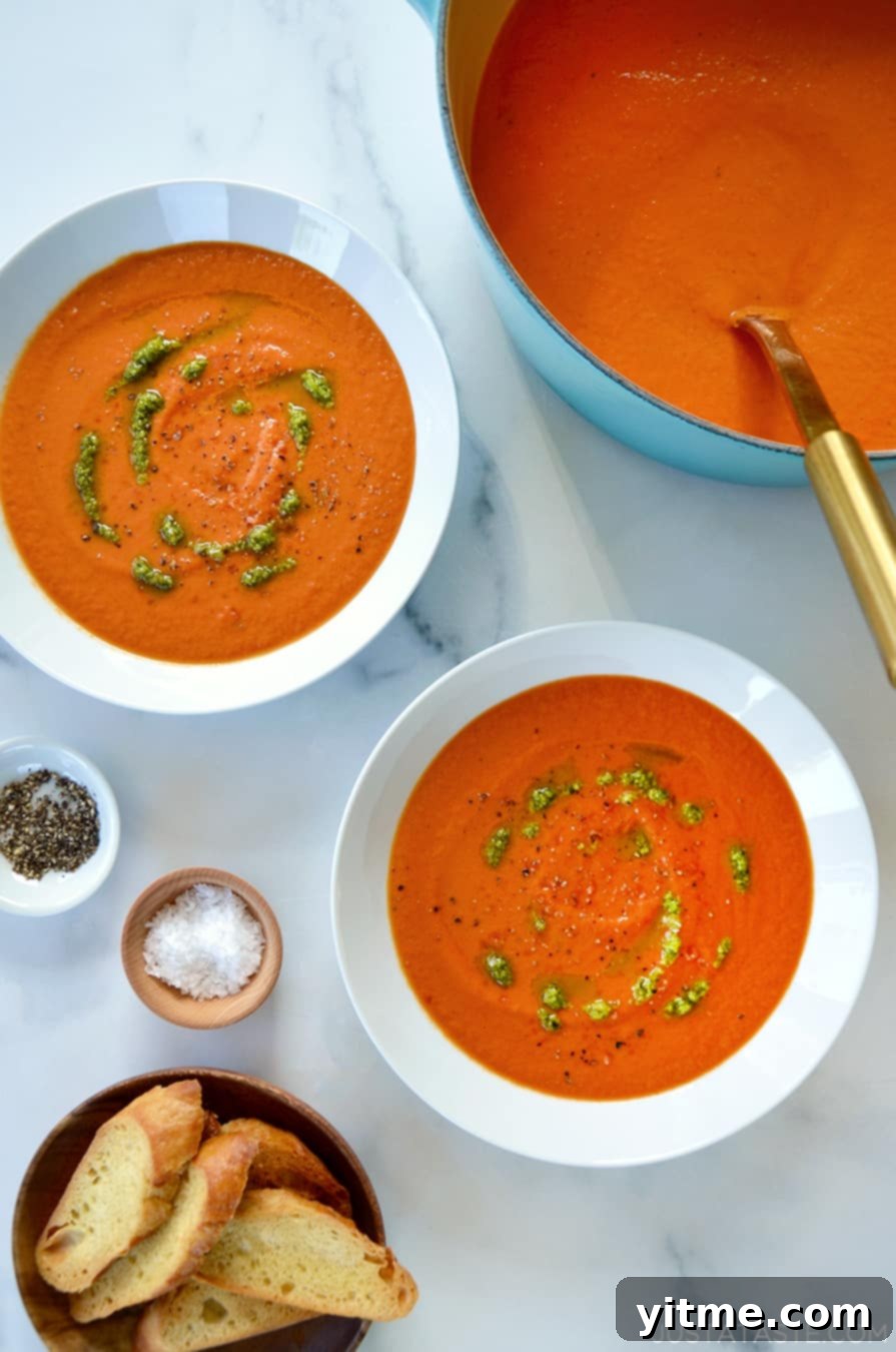 A teal stock pot of tomato soup with two white bowls filled with soup