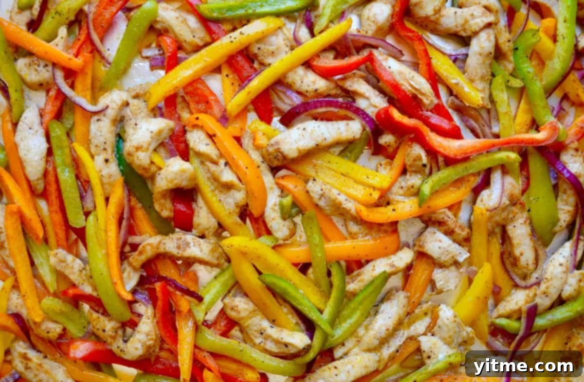 Cooked chicken strips with sliced red, green, yellow and orange bell peppers, and sliced red onion.