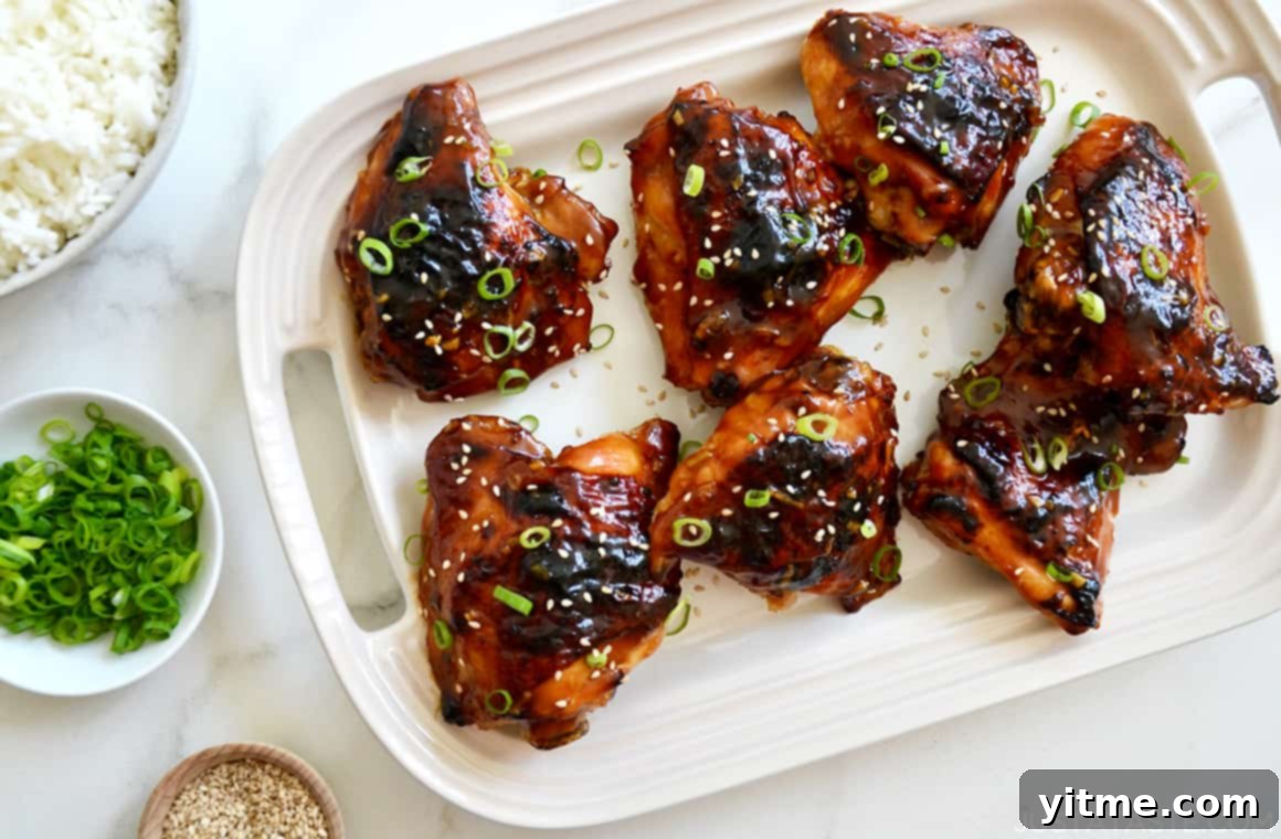 Glazed Honey Soy Chicken Thighs on a serving plate garnished with sesame seeds and sliced scallions