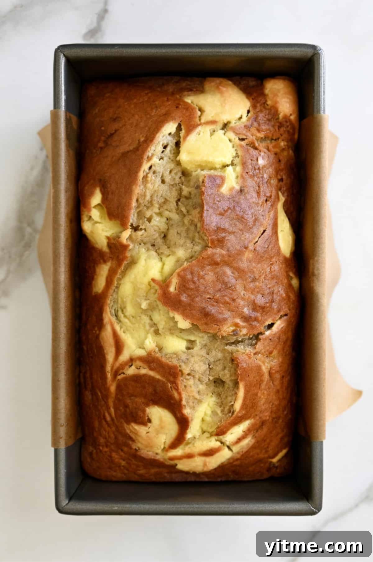 A perfectly baked loaf of cream cheese banana bread in a parchment paper-lined loaf pan.