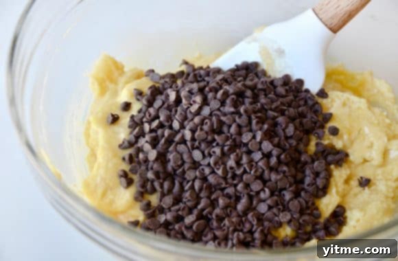 Mini chocolate chips in a glass bowl beside cookie dough and a spatula