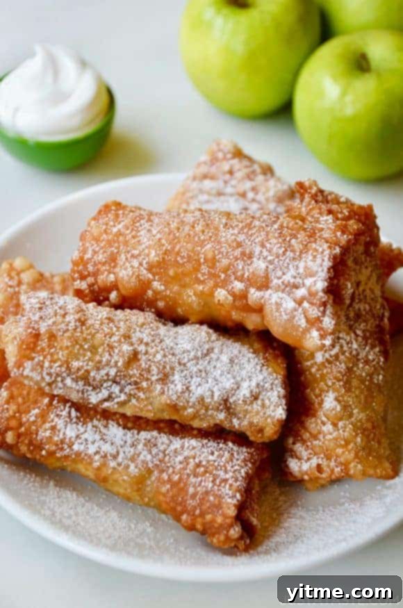 Golden Apple Pie Egg Rolls on a White Plate with Fresh Apples and Whipped Cream