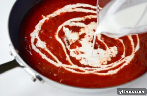 Tomato sauce in a pan with heavy cream being poured in