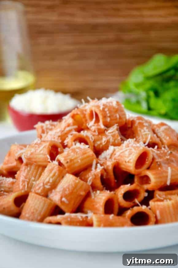 A white plate with vodka pasta on it and a salad in the background
