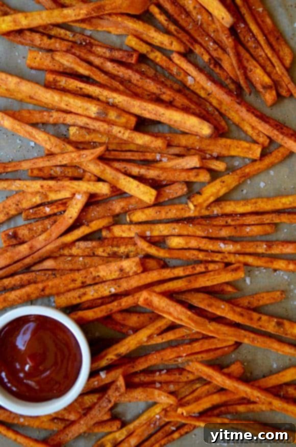 Baked sweet potato fries on a baking sheet with a bowl of ketchup