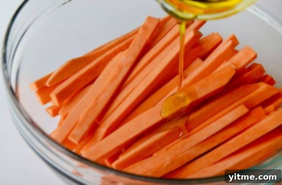Cut sweet potato fries in a glass bowl with olive oil drizzled on top