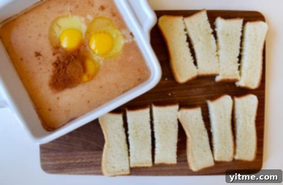 Slices of Texas toast cut into sticks, alongside a shallow dish filled with whisked eggs and milk, ready for dipping.