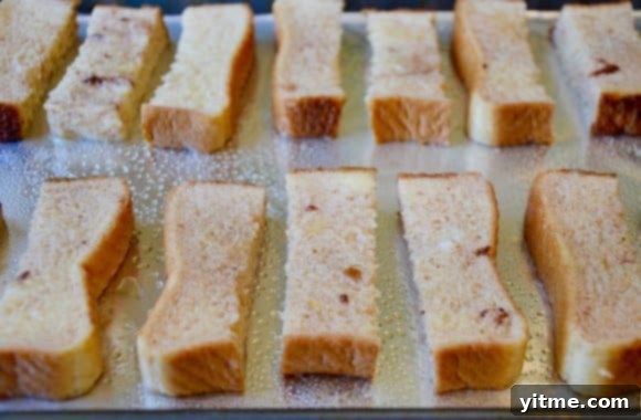 Perfectly arranged French toast sticks on a foil-lined baking sheet, ready to be baked to golden perfection.