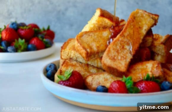Close-up shot of baked French toast sticks and fresh fruit artfully arranged on plates, with maple syrup for dipping, highlighting the textures and colors.