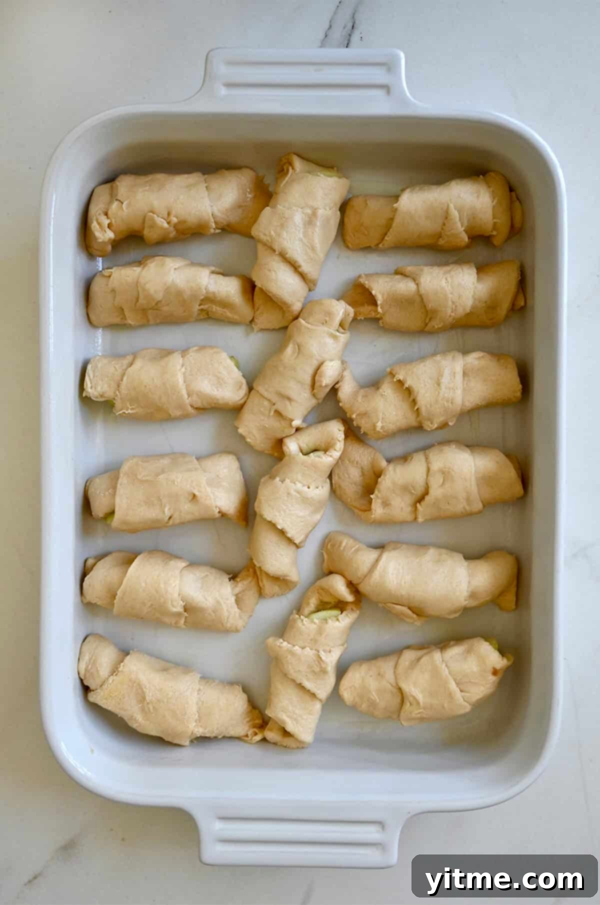 Apple Dumpling Delights: A Crescent Roll Twist 8 Unbaked crescent roll apple dumplings arranged in a 13x9-inch baking dish before adding sauce.