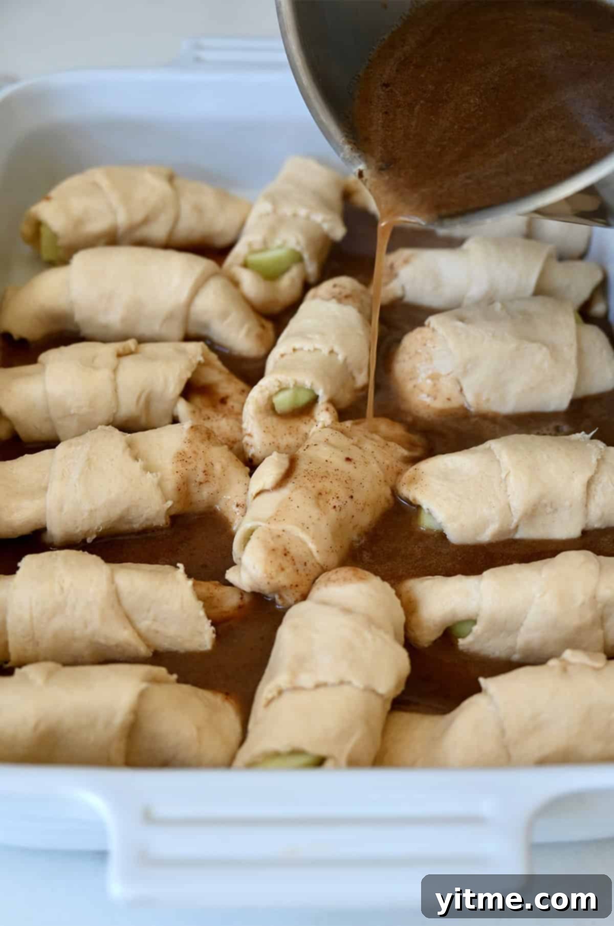 Apple Dumpling Delights: A Crescent Roll Twist 9 Brown sugar and butter sauce being poured over crescent roll apple dumplings before baking.