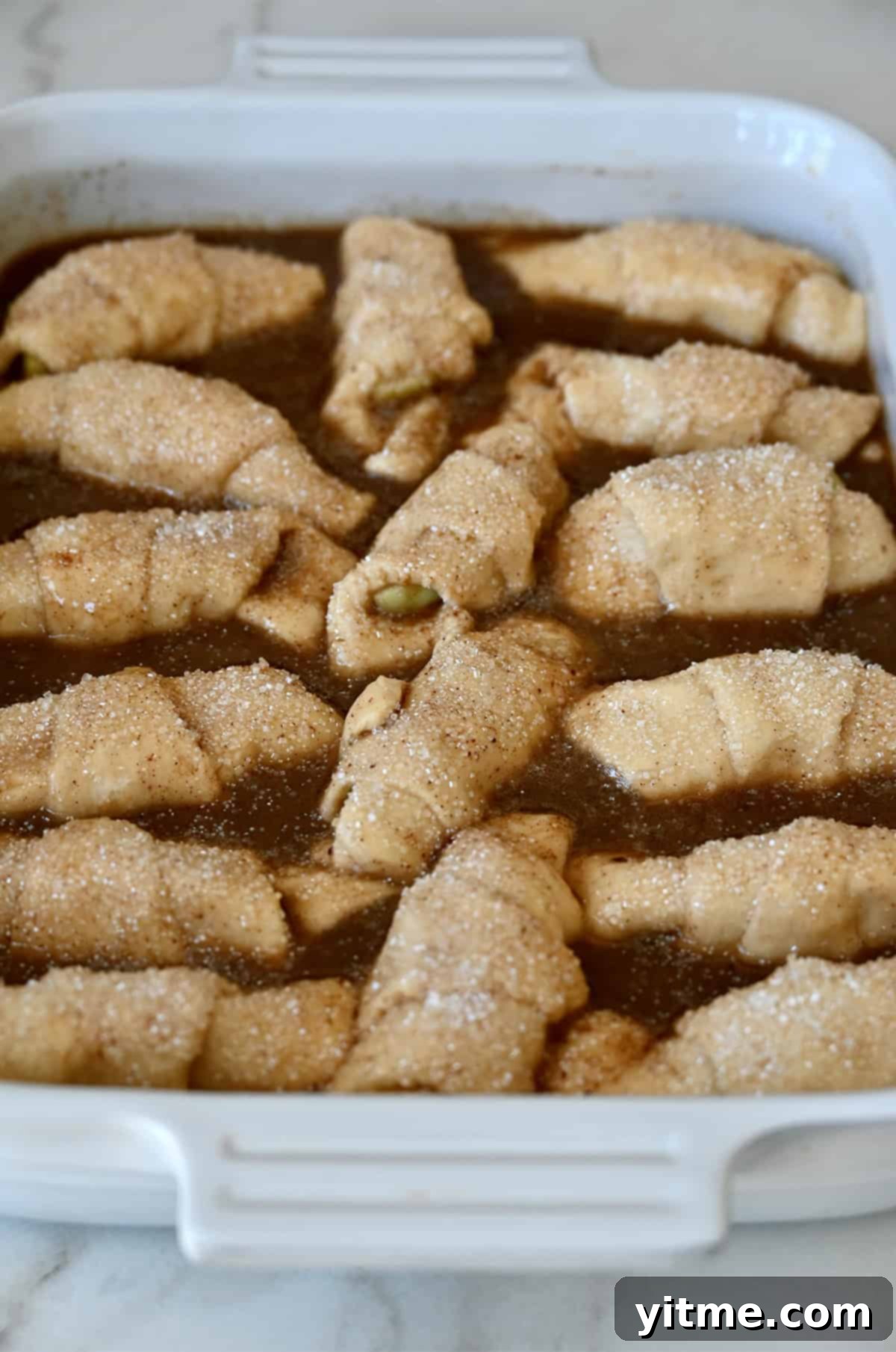 Apple Dumpling Delights: A Crescent Roll Twist 10 Crescent roll apple dumplings in caramel sauce before going into the oven to bake.
