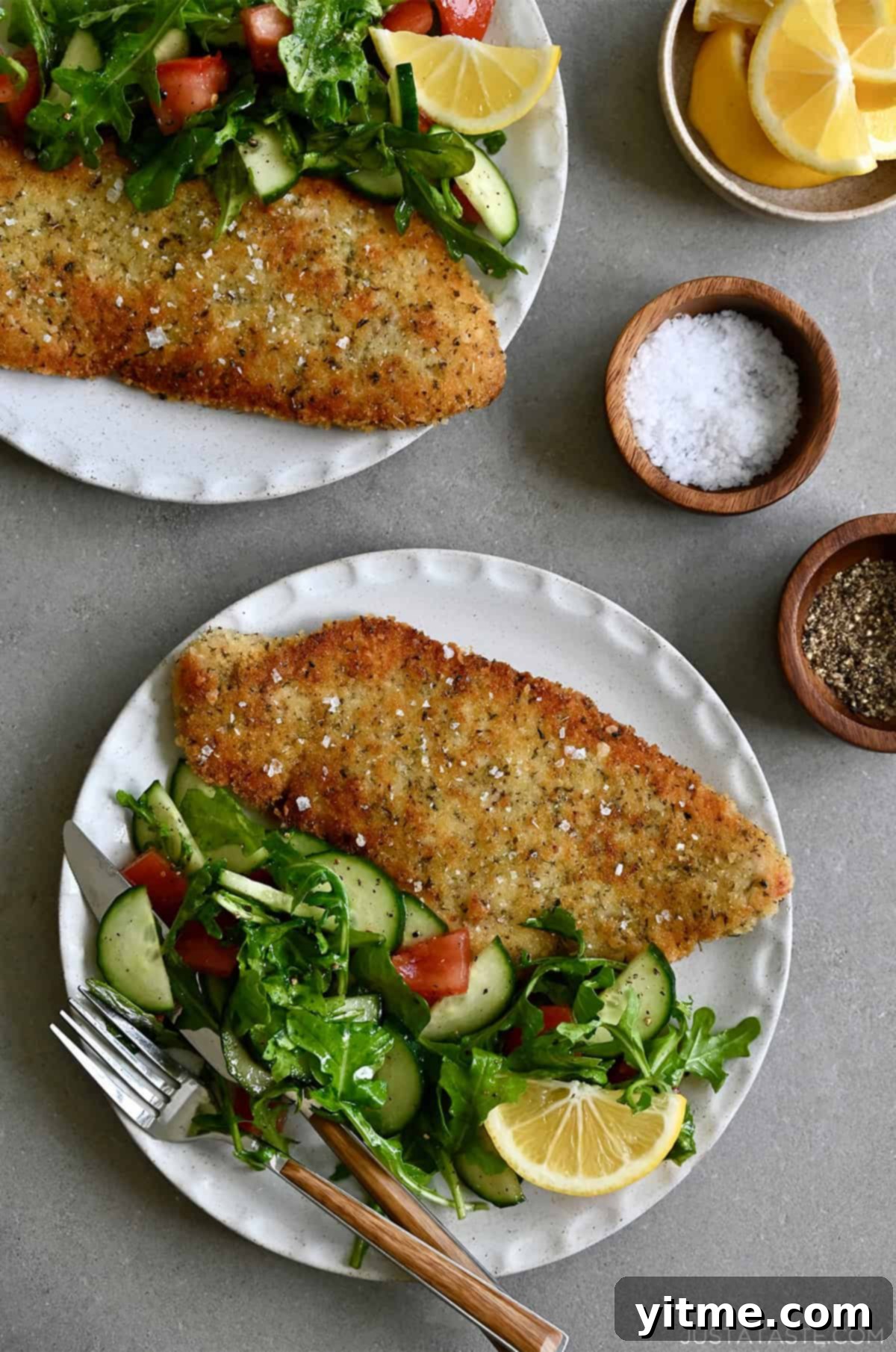 Hungarian-Spiced Crispy Cutlets 2 Wiener schnitzel (crispy veal cutlet) on a dinner plate with a side salad and a fork.