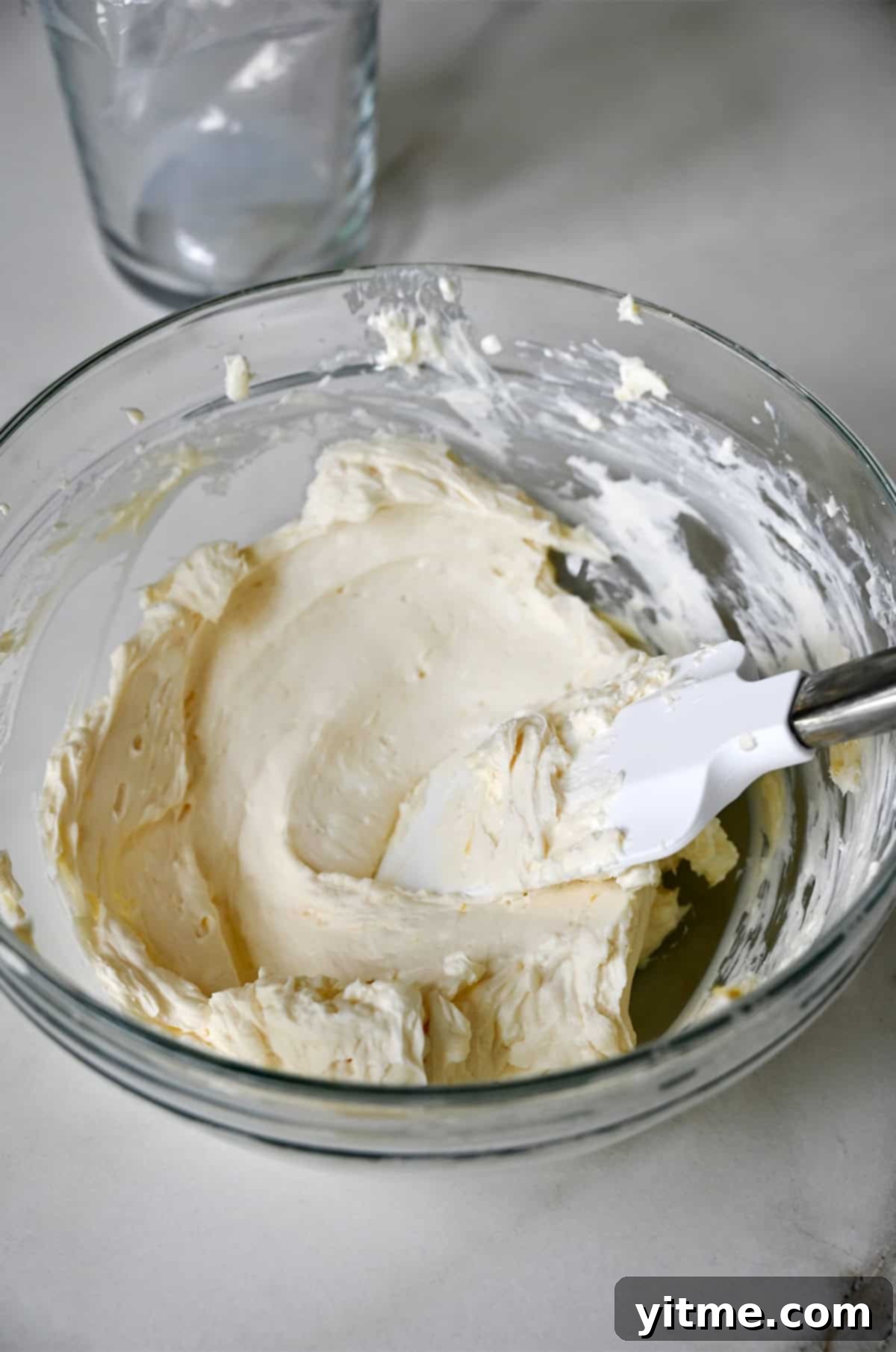 Lemon cream cheese in a glass bowl with a spatula, showcasing the smooth texture of the filling.