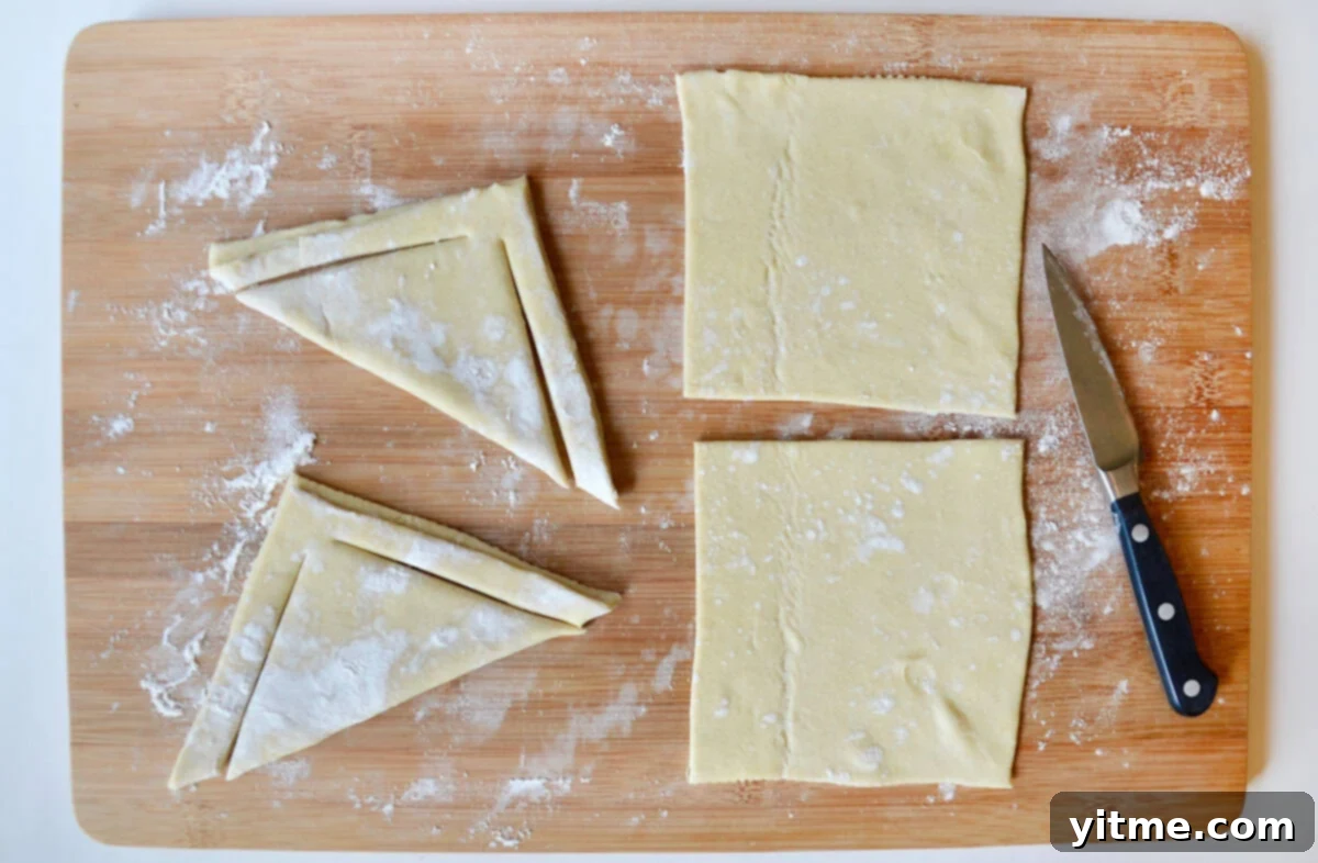 Two triangle-shaped puff pastry dough with slits next to two squares of puff pastry dough on a cutting board with a sharp knife, demonstrating the cutting technique.