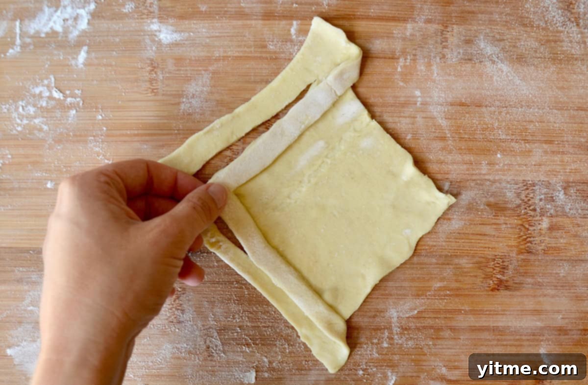 A hand folds puff pastry to form a diamond shape, illustrating the criss-cross technique.