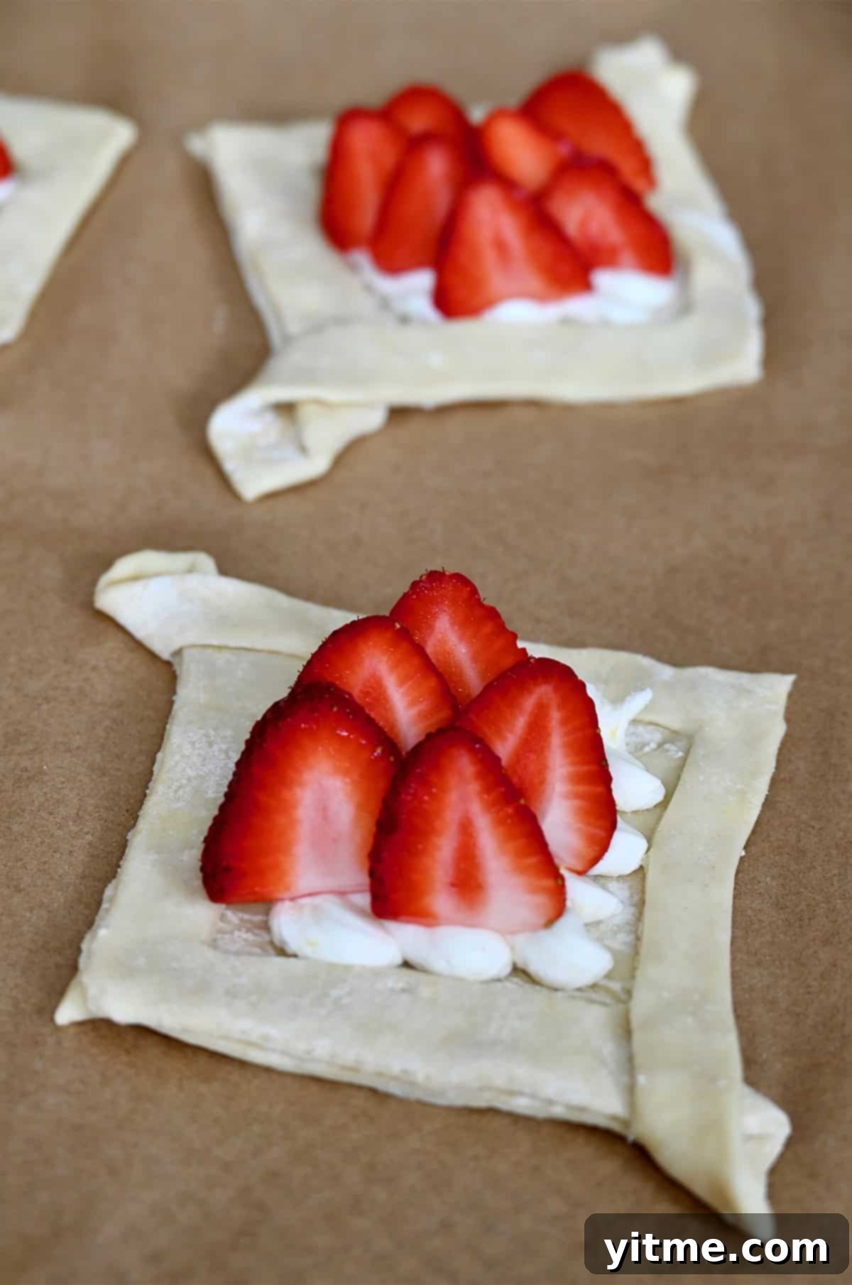 Unbaked cheese Danish topped with fresh strawberries on parchment paper, ready for the oven.