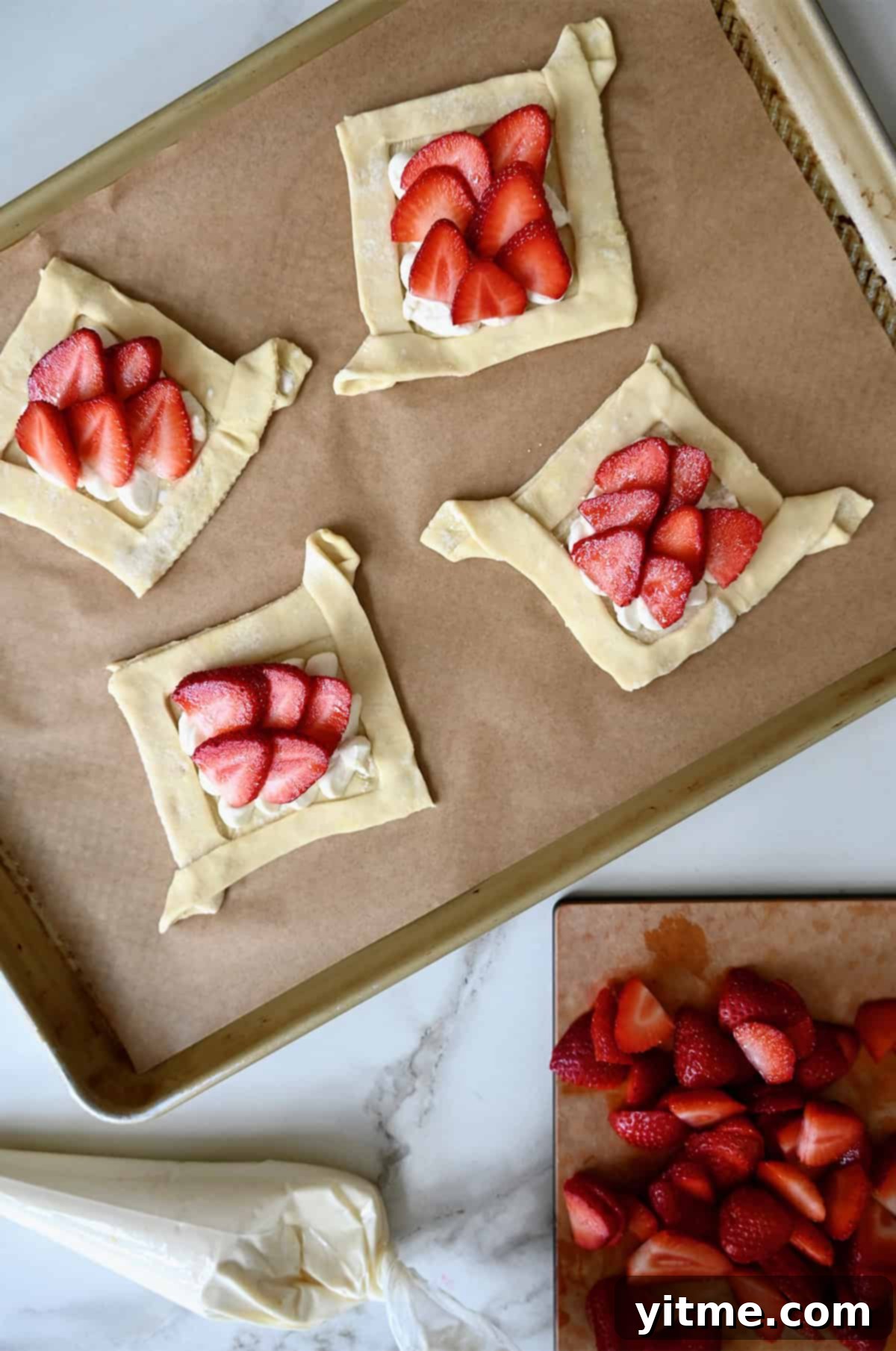 Unbaked strawberry cream cheese Danish on a parchment paper-lined baking sheet, showcasing the pre-baked appearance.