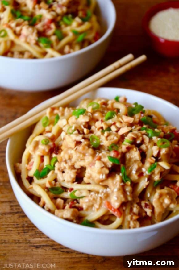 White bowl with chopsticks containing Dan Dan Noodles with Chicken, garnished with scallions