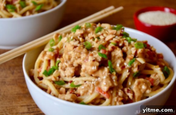 Dan Dan Noodles with Chicken in white bowl with chopsticks, garnished with fresh scallions, ready to be enjoyed