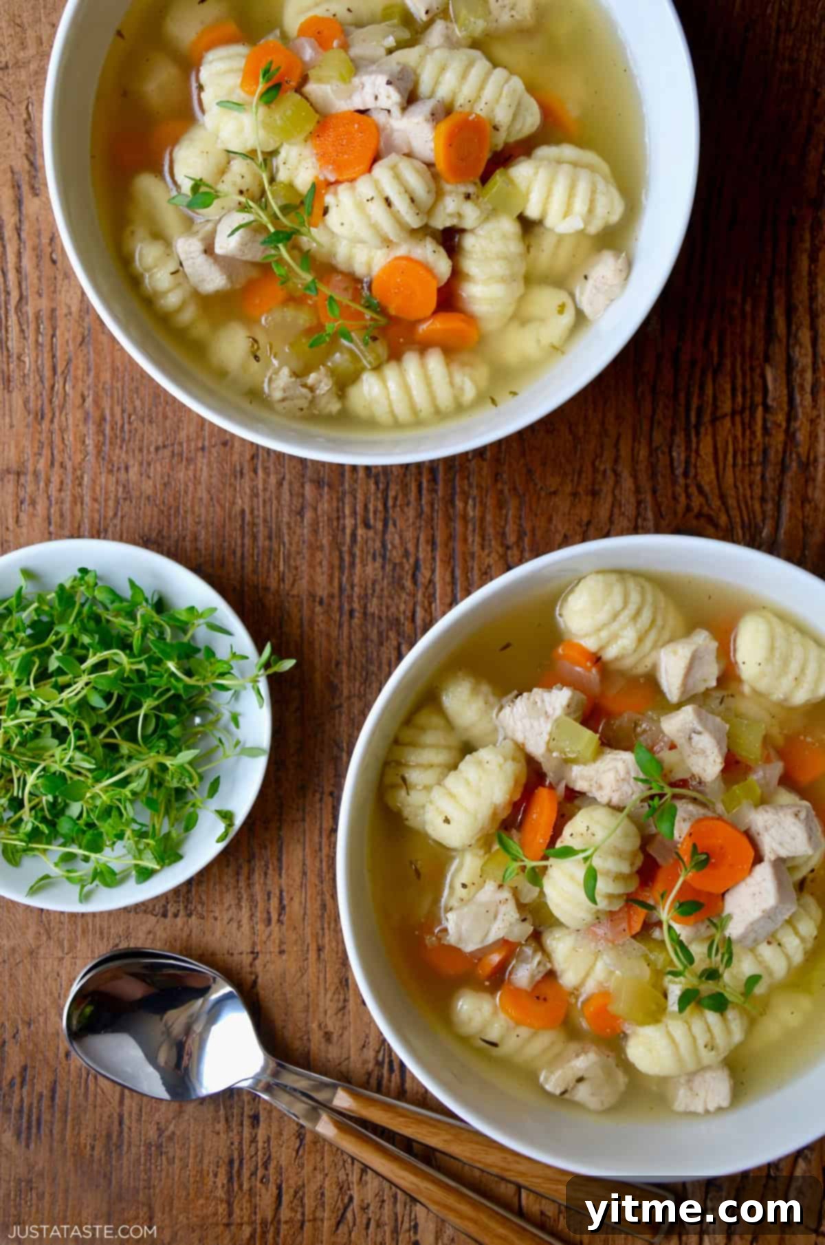 Two bowls of homemade chicken gnocchi soup topped with fresh thyme sprigs, showcasing golden broth, tender chicken, and soft gnocchi.