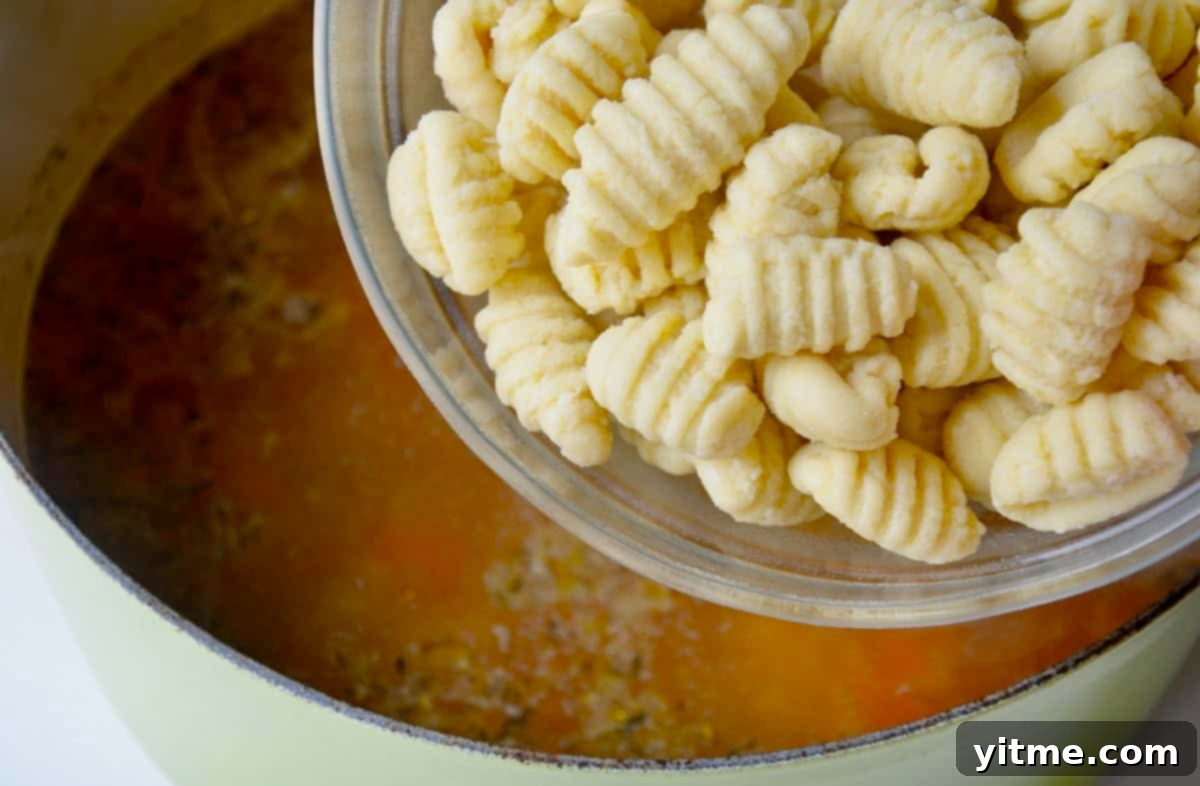 Adding store-bought gnocchi to a stockpot with broth and sauteed aromatics to make a homemade soup.