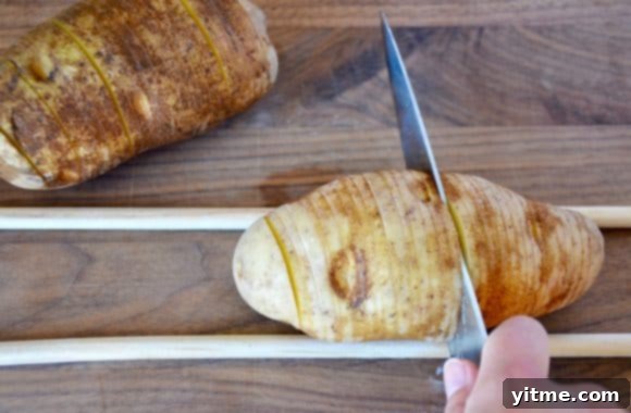 Close-up shot of slicing Hasselback potatoes on a wooden cutting board using two wooden spoons as guides.
