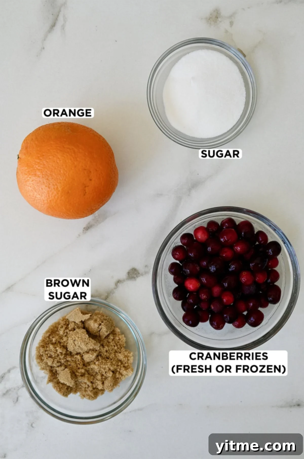 An orange next to three bowls containing white granulated sugar, fresh cranberries, and brown sugar, the four key ingredients for homemade cranberry sauce.