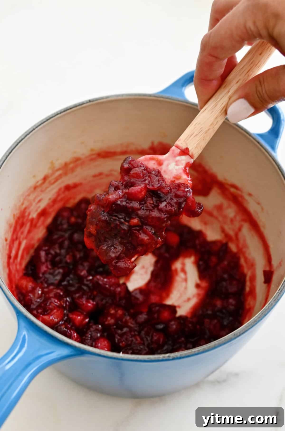 Homemade cranberry sauce is thickened enough to coat a spatula, showing the perfect jammy consistency after cooking.