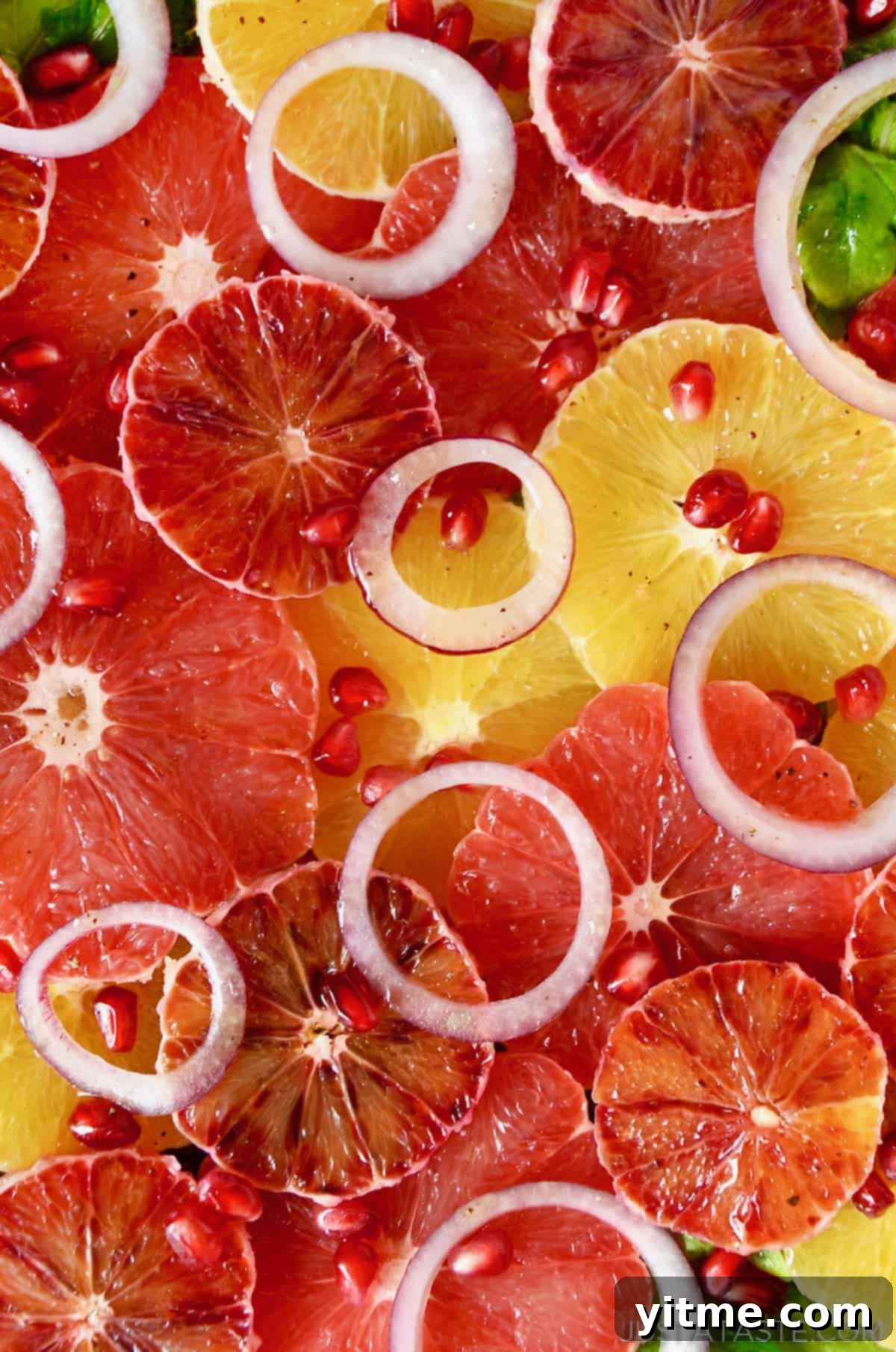 A salad made up of layers of sliced oranges, blood oranges and grapefruits, red onion slices, arugula and pomegranate seeds.