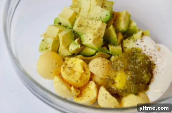 A clear bowl filled with cooked egg yolks, mustard, avocado, mayo and relish