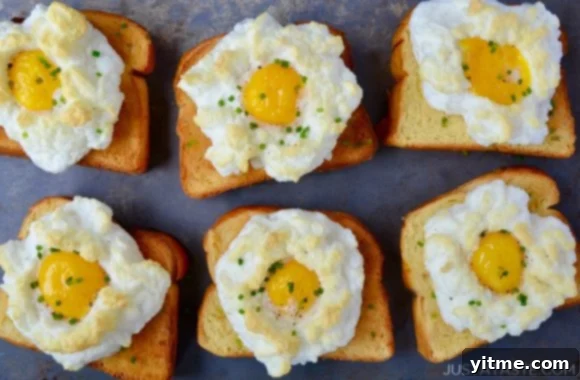A silver baking sheet holds two elegant Cloud Eggs, with their fluffy white clouds and bright yellow yolks, served on top of toasted brioche.