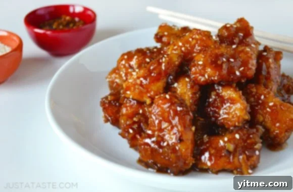 A white plate showcasing succulent Baked Orange Chicken, garnished with fresh herbs, alongside a pair of chopsticks.