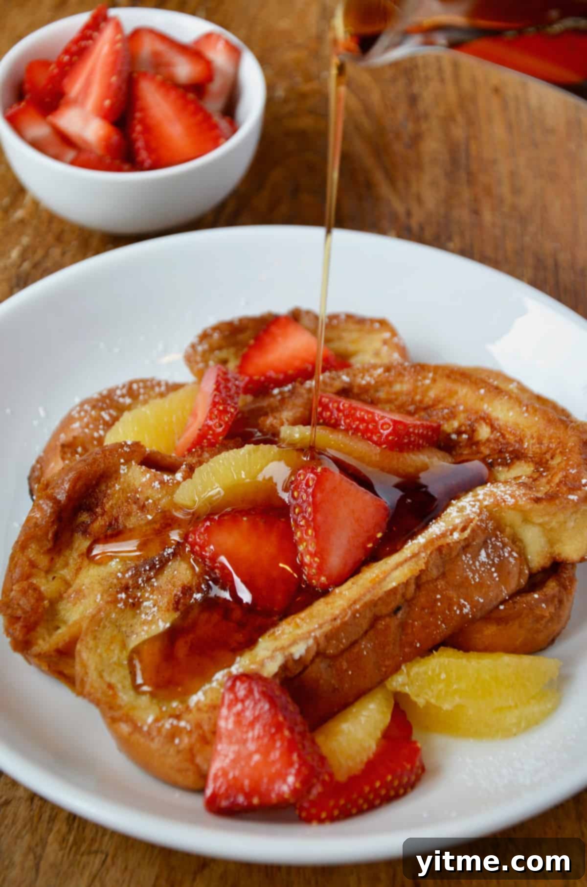 Challah French toast topped with strawberries and orange segments, drizzled with maple syrup