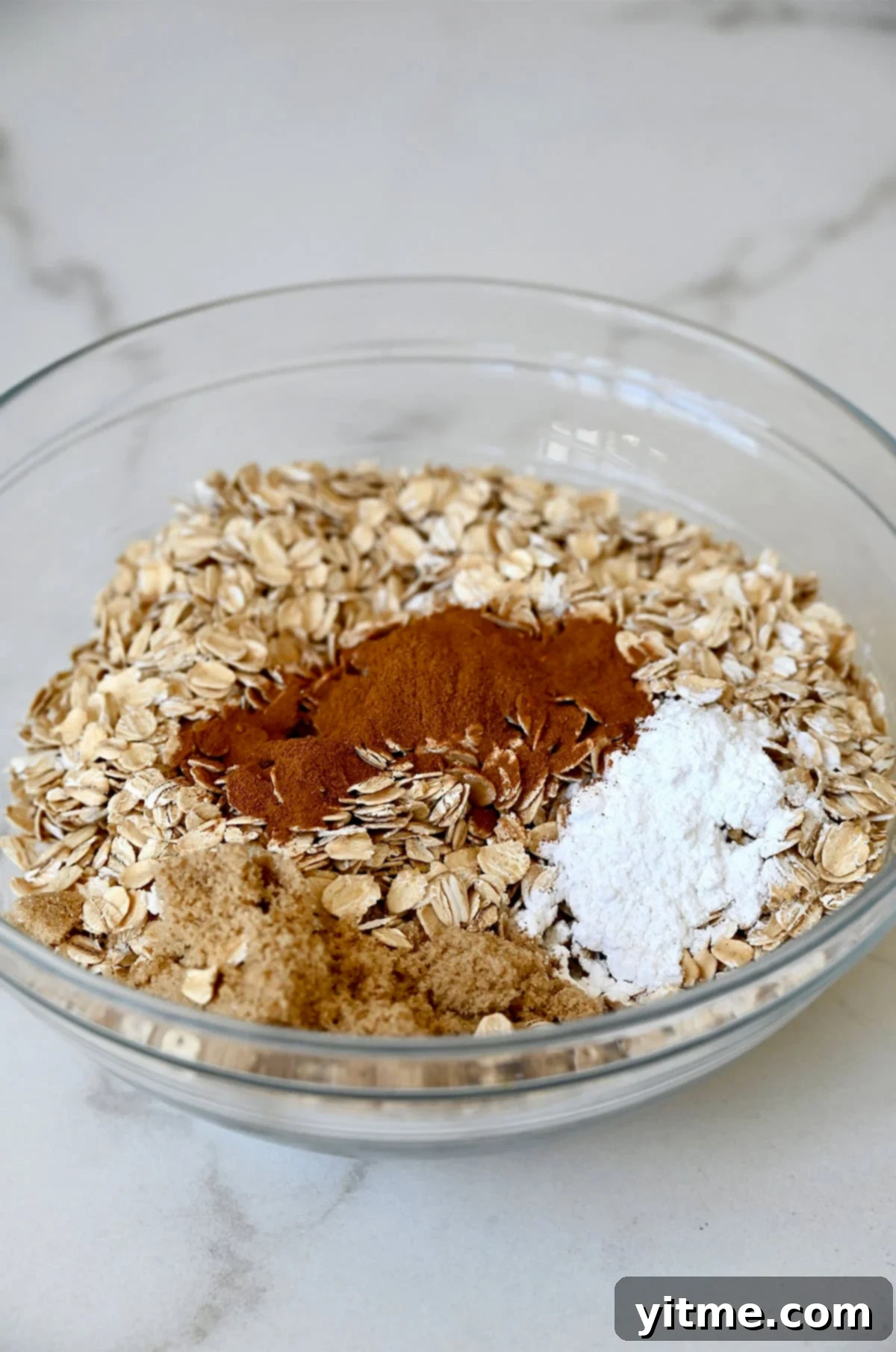 Rolled oats, cinnamon, brown sugar and baking powder in a glass bowl.