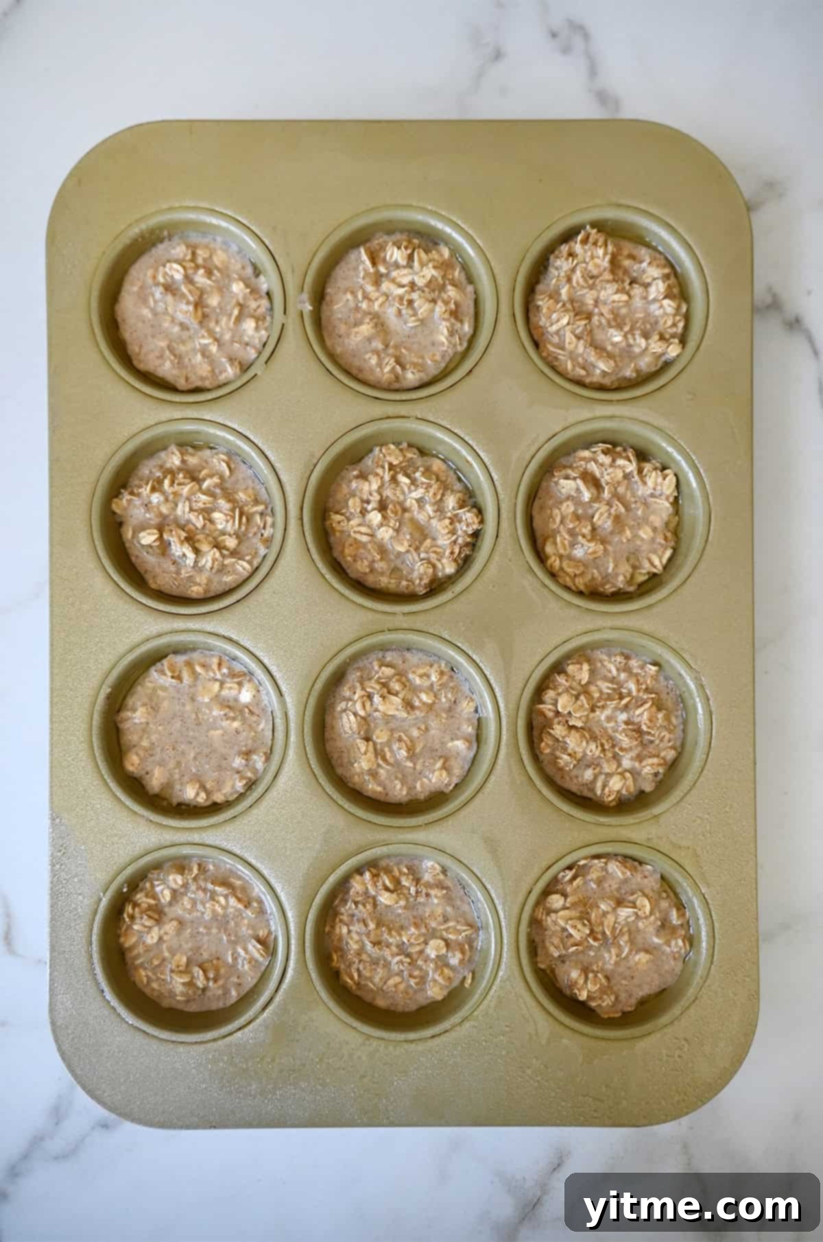 A muffin pan filled with an oatmeal mixture featuring mashed bananas, milk and cinnamon.