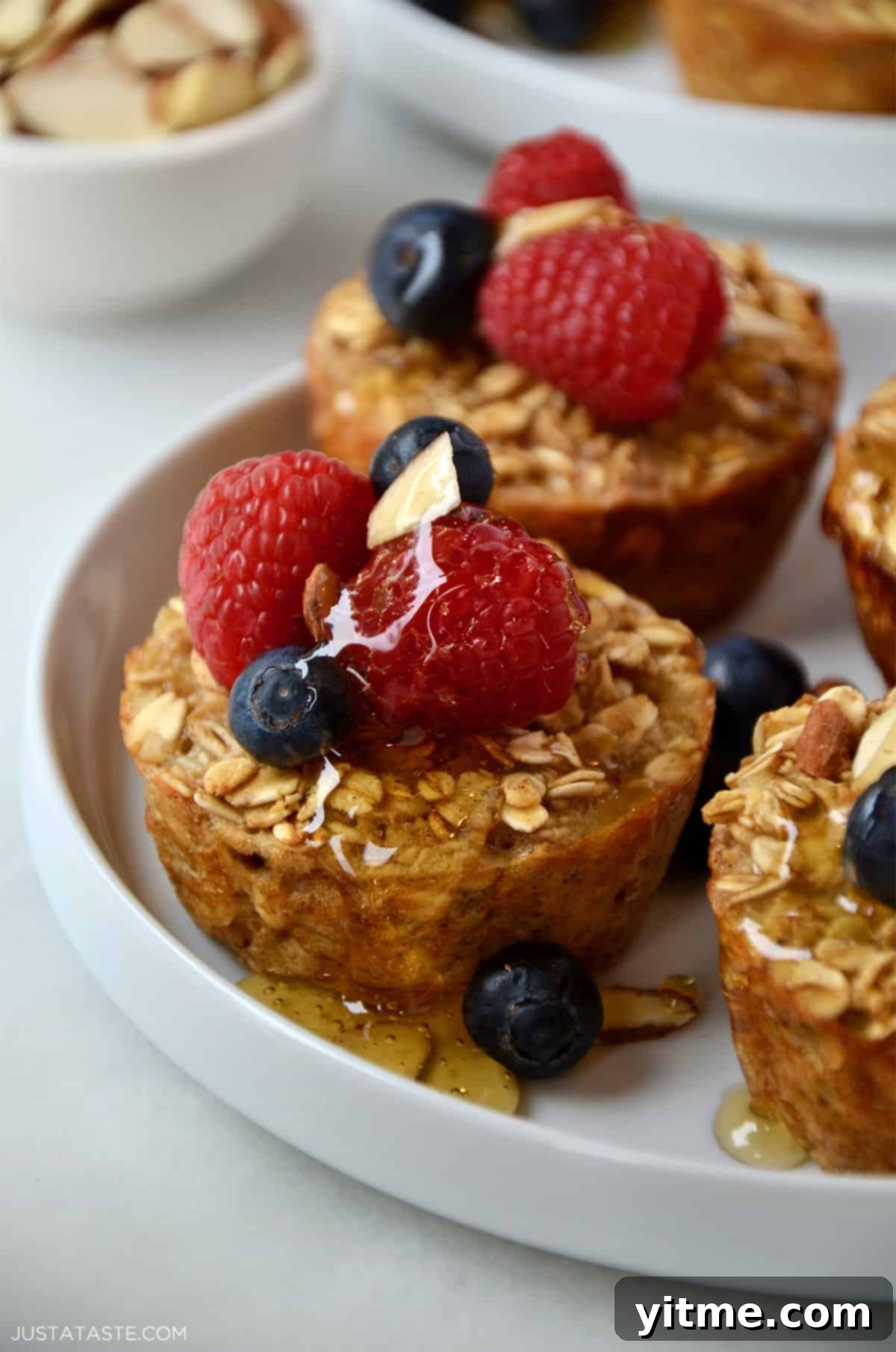 Baked oatmeal muffins drizzled with warm maple syrup and topped with fresh berries and sliced almonds.