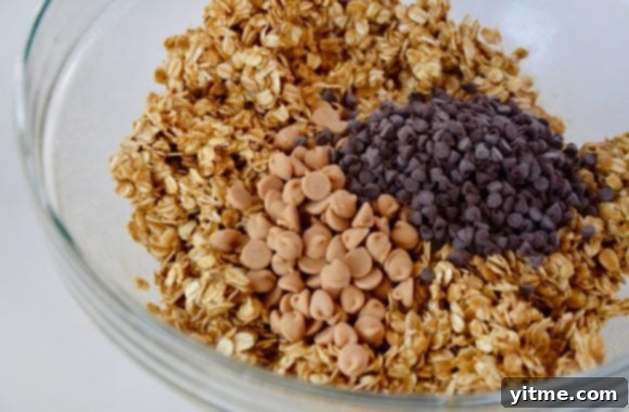 A clear glass bowl holding a perfectly blended oat mixture, generously studded with vibrant peanut butter chips and decadent mini chocolate chips, ready for baking.