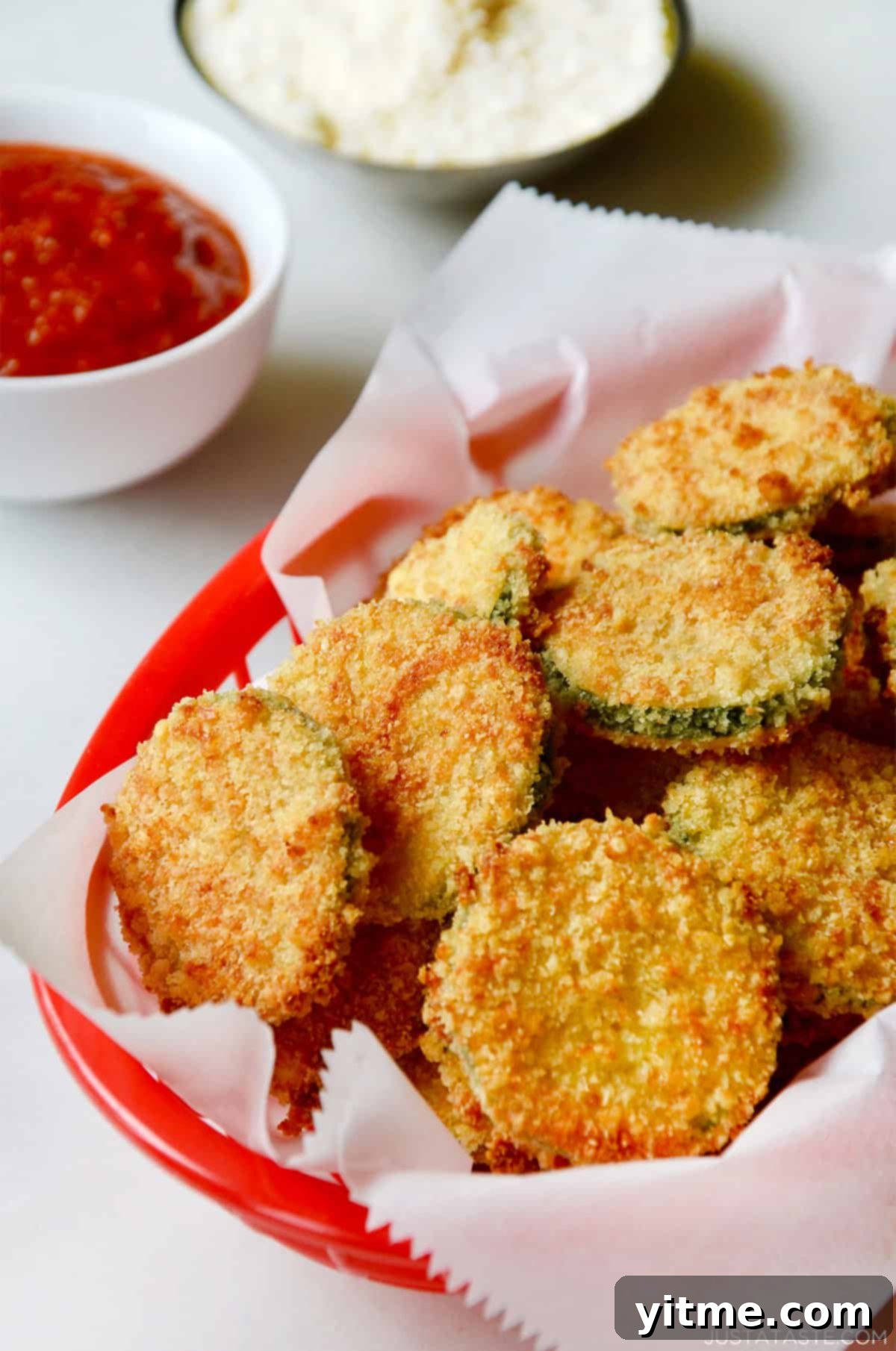 Baked zucchini chips with parmesan in a red food basket lined with parchment paper.