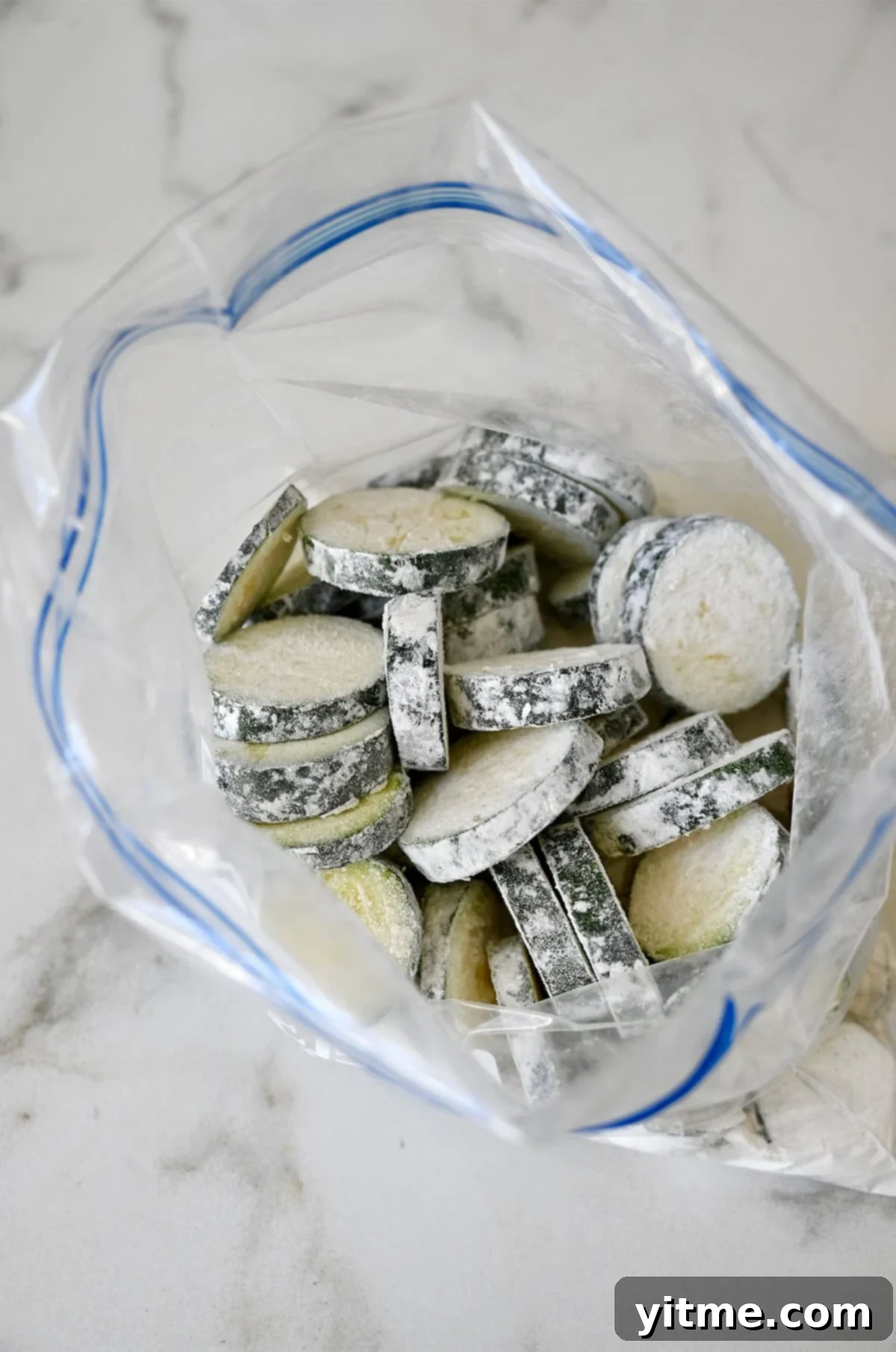 Slices of zucchini coated in flour in a plastic ziplock bag.