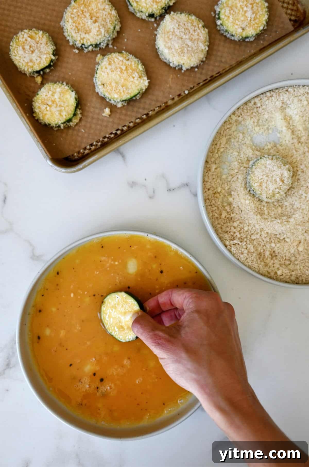 Breading station for dredging zucchini chips, which includes a shallow bowl containing whisked eggs and another shallow bowl with Panko breadcrumbs.