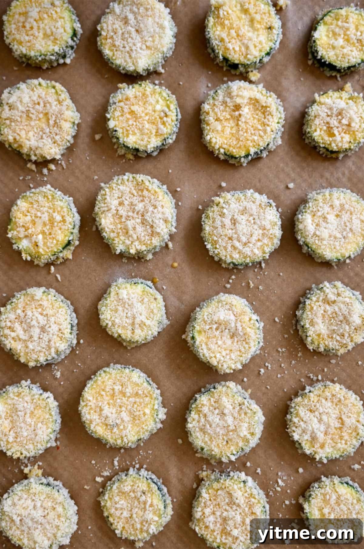 Breaded zucchini chips with parmesan on a parchment paper-lined baking sheet.