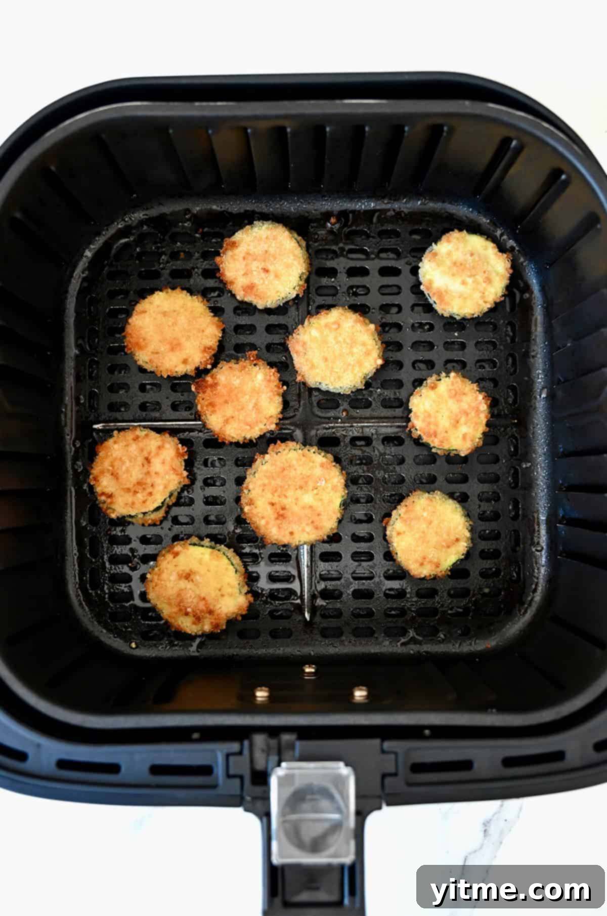 Golden brown, crispy air fryer zucchini chips in the basket of an air fryer.