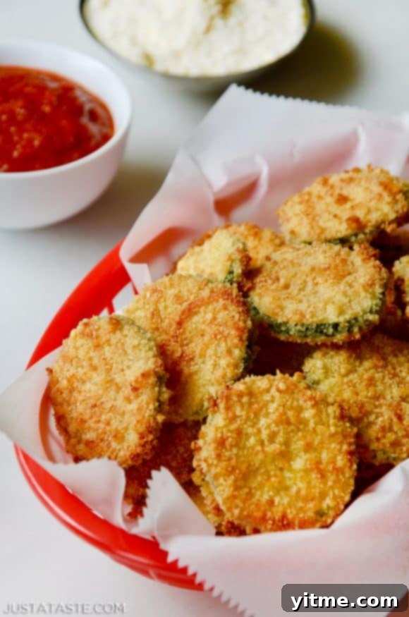 Baked Parmesan Zucchini Chips in red basket lined with white food paper with ketchup and mayonnaise in the background.
