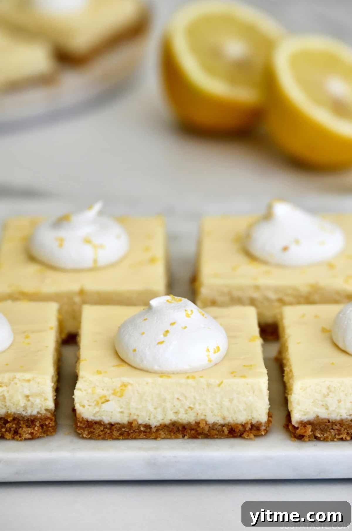 Easy cheesecake bars topped with whipped cream and lemon zest on a white platter.
