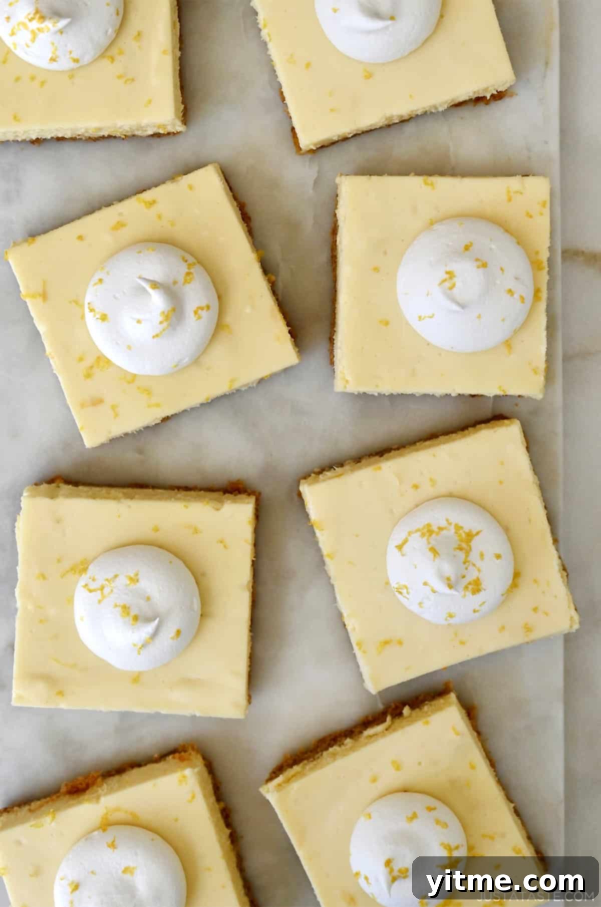 Creamy lemon cheesecake bars topped with a dollop of whipped cream and lemon zest.