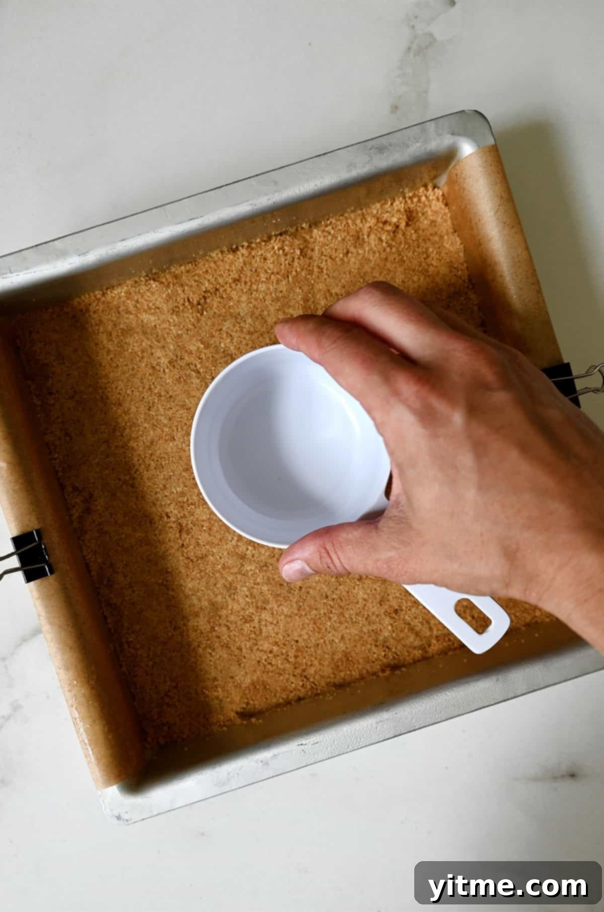 Pressing graham cracker crust into a baking dish by using the bottom of a measuring cup.