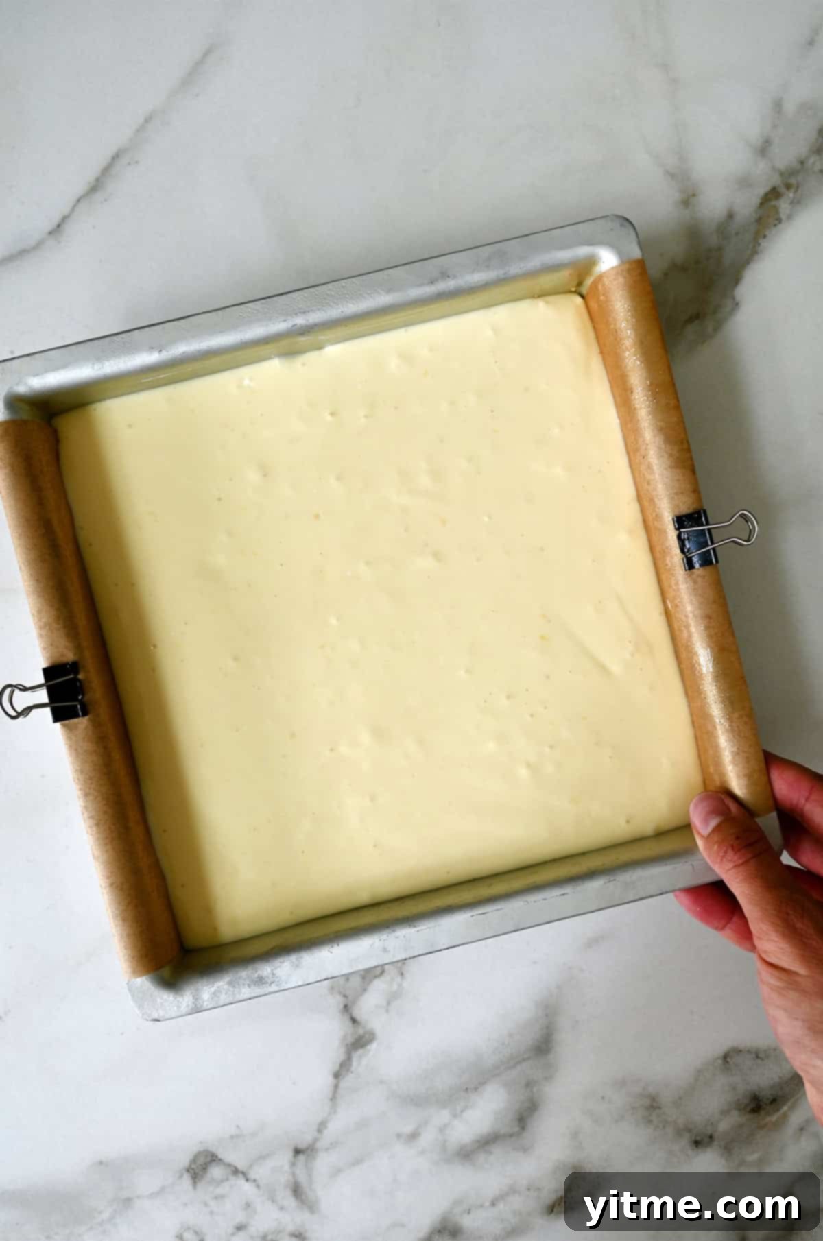 Unbaked cheesecake bars in a parchment paper-lined baking dish.