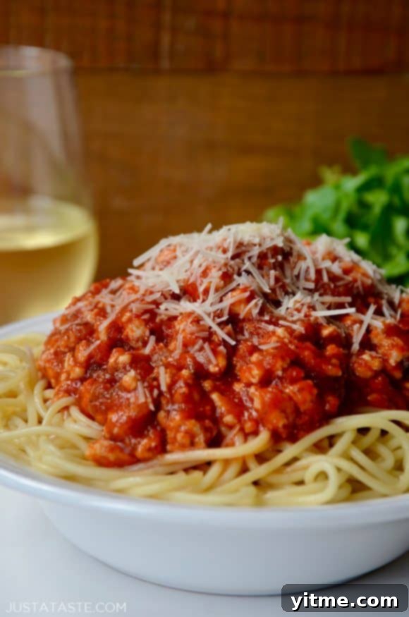 Quick Spaghetti Bolognese with Turkey garnished with shredded Parmesan cheese in white bowl with glass of white wine in background