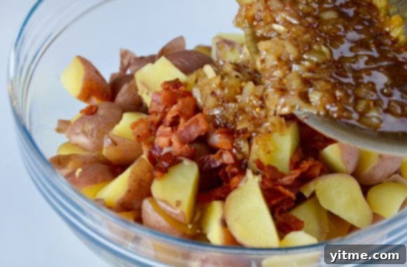 Glass bowl with quartered red potatoes and cooked bacon with warm bacon dressing being poured on top. 